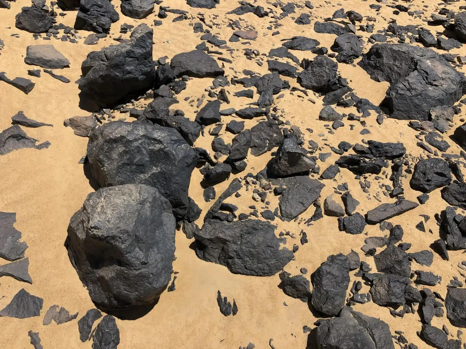 Dark volcanic rocks scattered across sand in Black Desert Egypt
