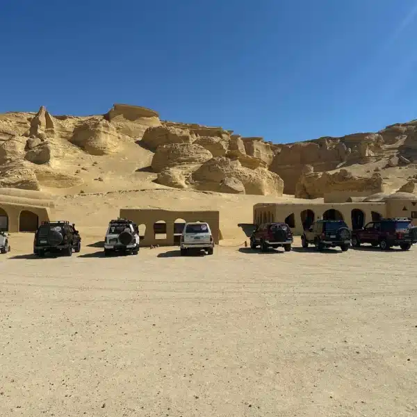 Four-wheel-drive safari vehicles beside the rock formations of Wadi Al-Hitan