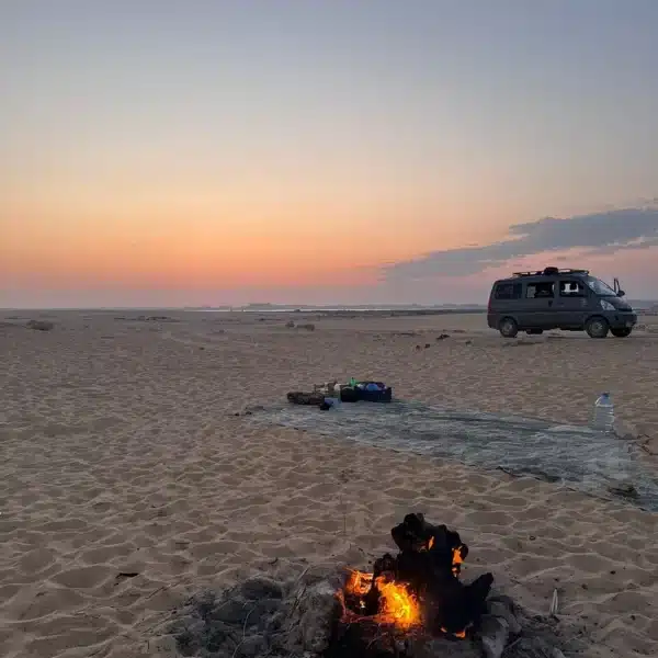 Campfire and 4x4 vehicle on the Siwa desert at sunset